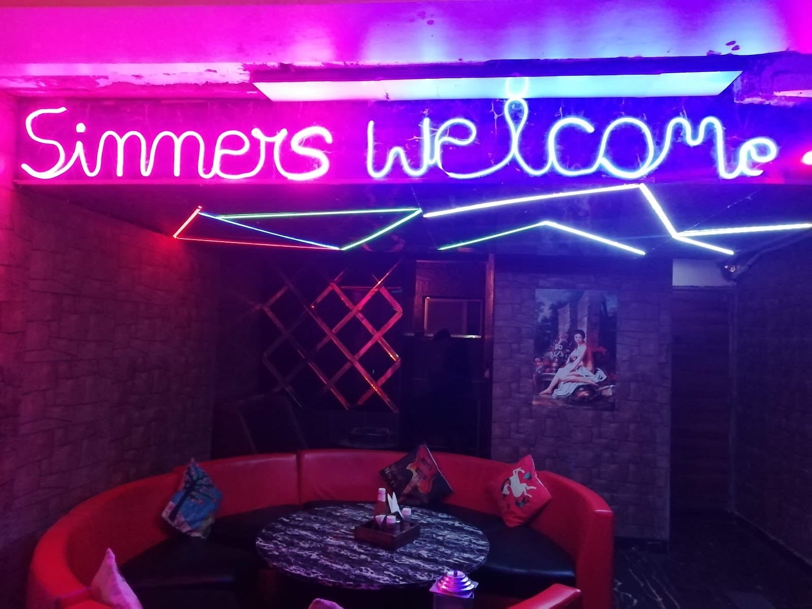 Neon “Sinners welcome” sign above red lounge sofas