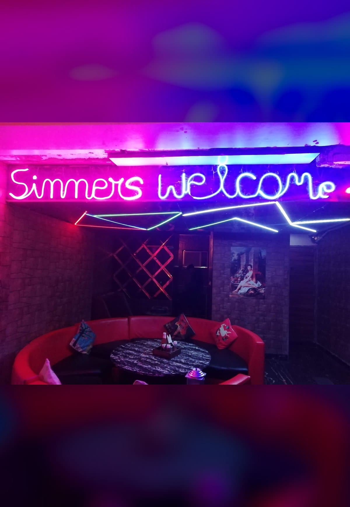 Inside Madira: a neon “Sinners welcome” sign over red lounge sofas